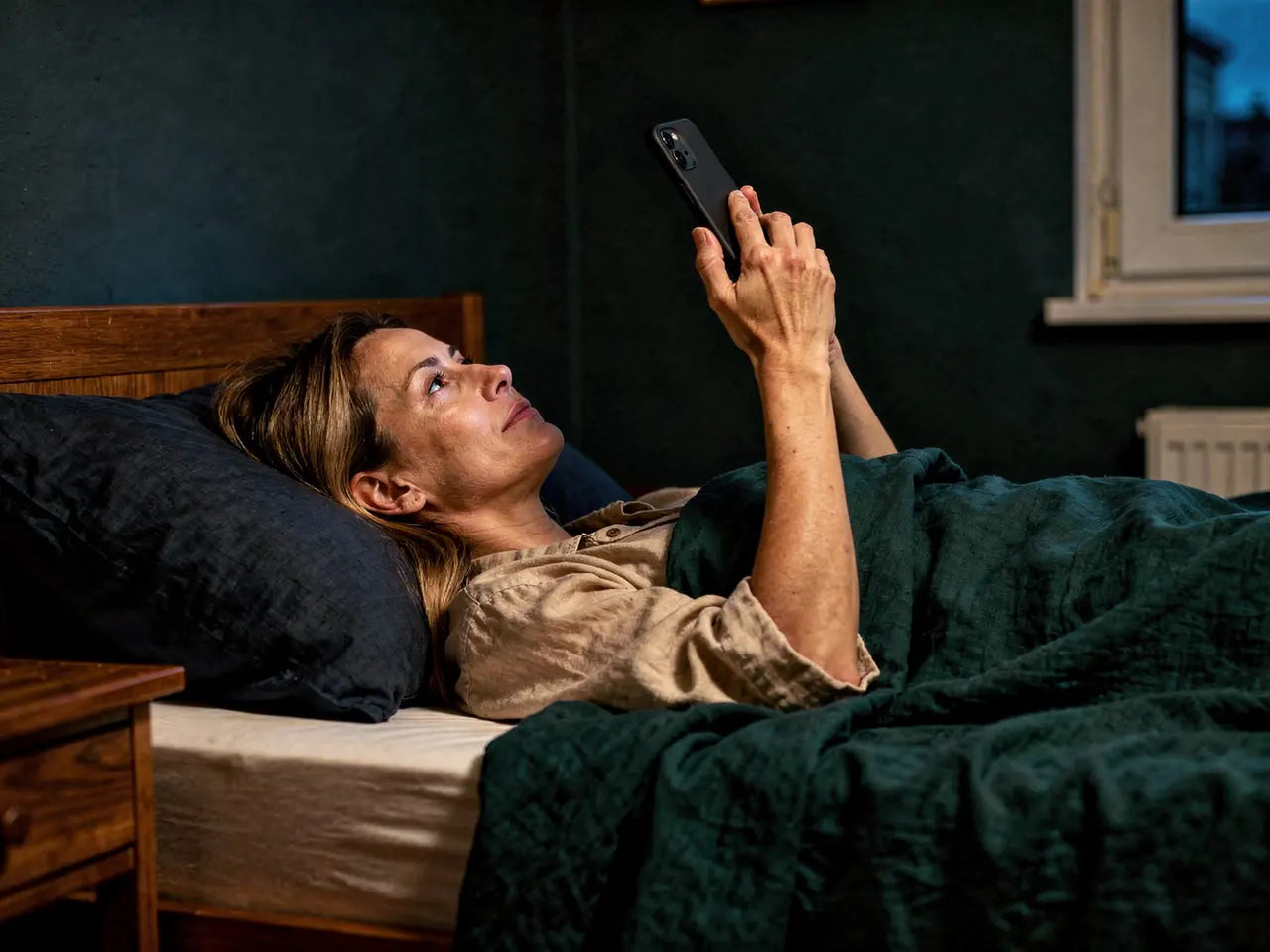 Frau liegt abends im dunklen Schlafzimmer, ihr Gesicht vom Handy beleuchtet