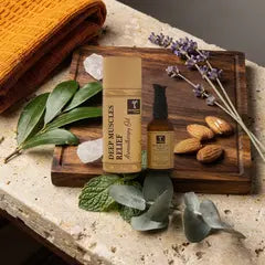 Abhyanga Muskel-Massageöl mit Hülse auf Holz, daneben Kampferblätter, Pfefferminze, Eukalyptus und Lavendel