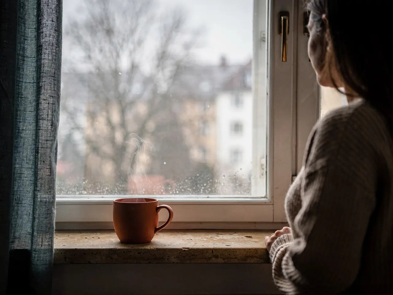 Nebliger grauer Morgen hinter einem Fenster, auf dem Fensterbrett eine Tasse