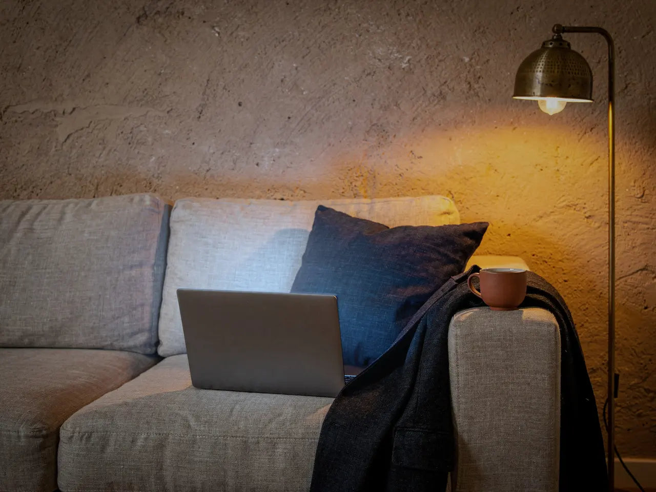 Aufgeklappter Laptop auf dem Sofa am späten Abend, daneben Tee und ein Blazer