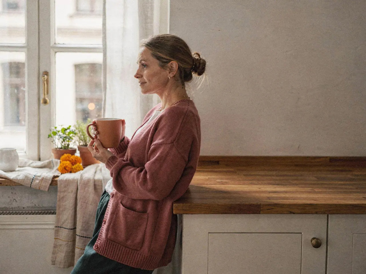 Frau hält in der Büroküche eine warme Tasse mit beiden Händen