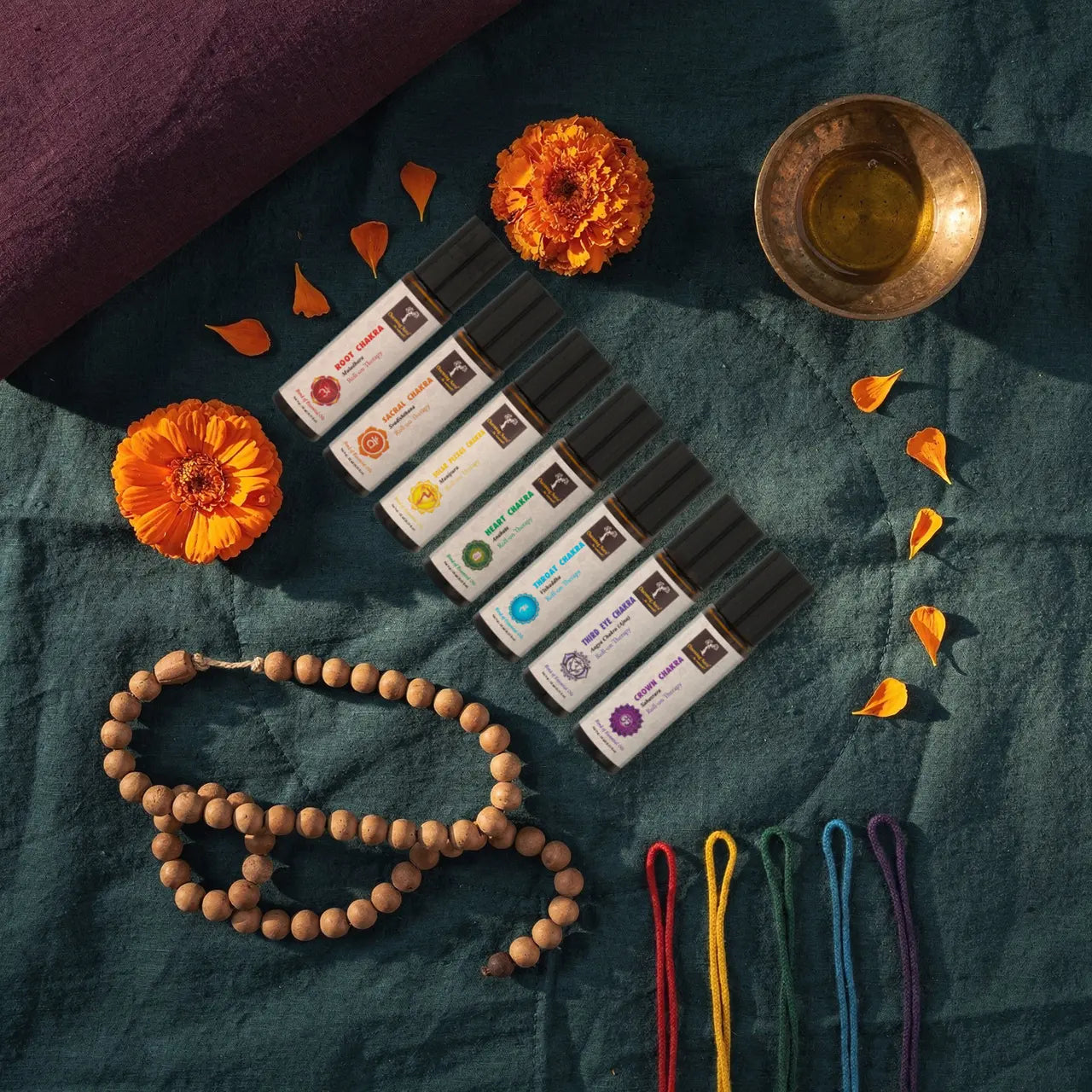 Sieben Chakra-Roll-ons in einer Reihe, vor jedem eine Baumwollkordel in seiner Farbe