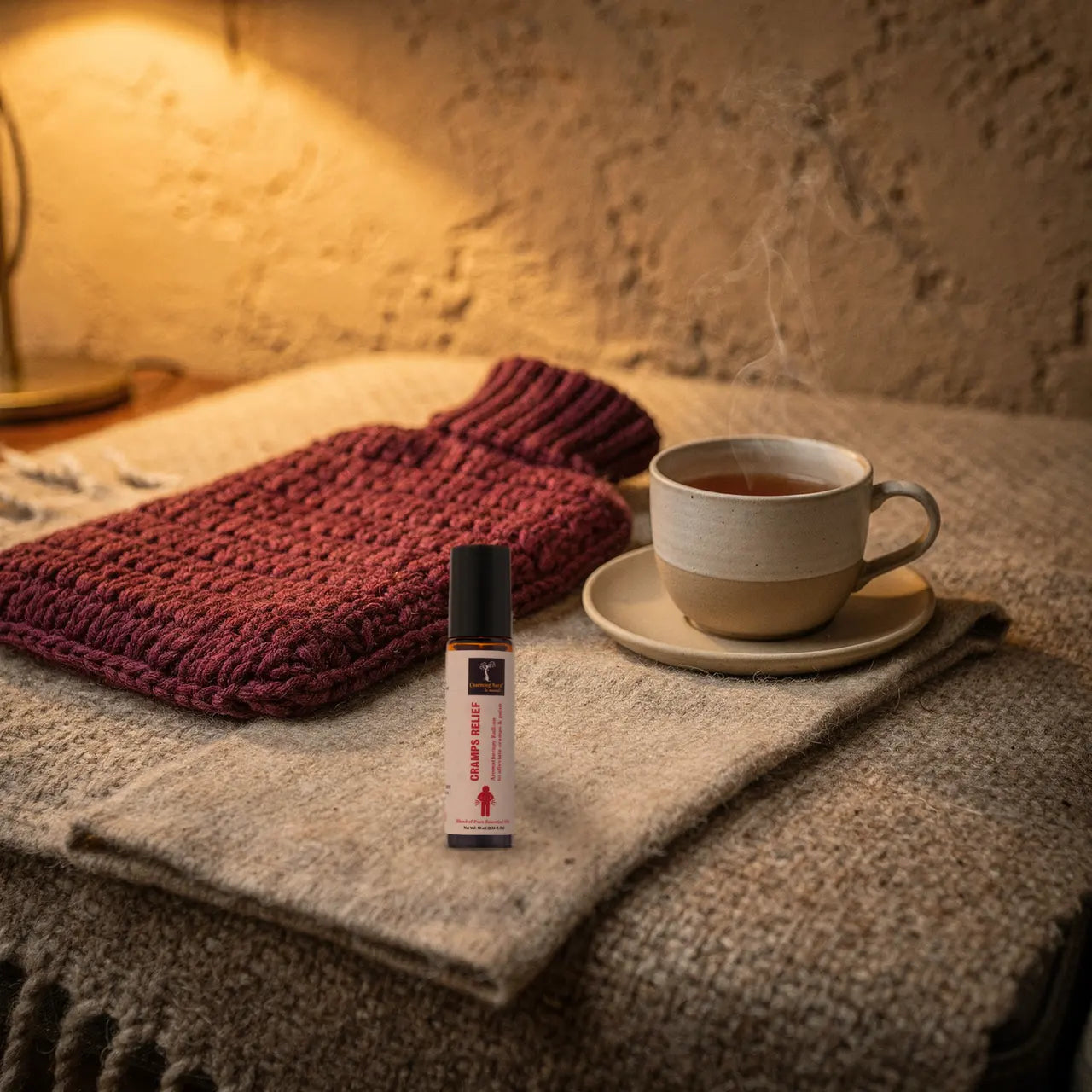 Hand hält Ushma Roll-on neben einer Teetasse und einer Wärmflasche
